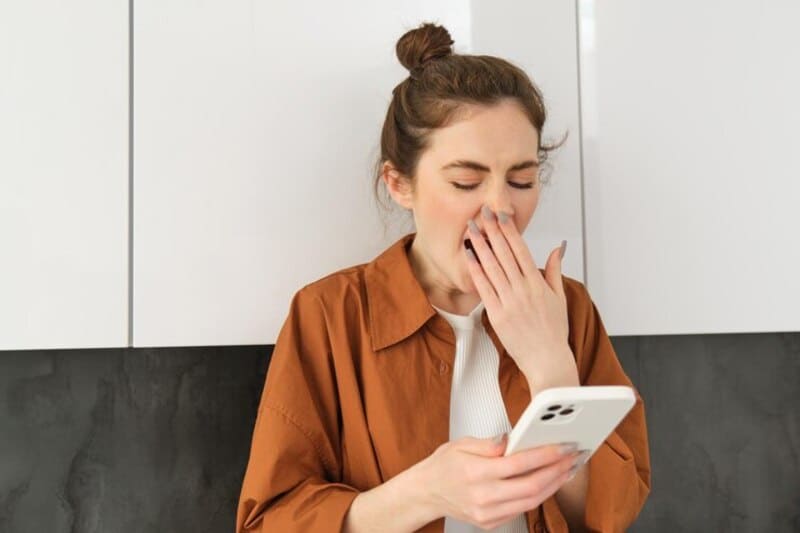 foto de mulher segurando o celular e bocejando